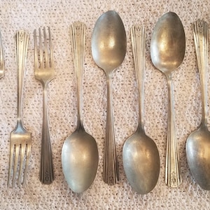 May include: A set of ten silver-plated forks and spoons. The forks have three tines and the spoons have a rounded bowl. The silverware is arranged in two rows, with the forks on top and the spoons on the bottom.