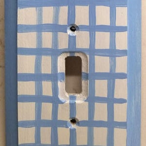 May include: A light blue wooden light switch cover with a white and light blue checkered pattern.