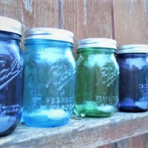 May include: A row of vintage Ball mason jars in various shades of blue and green, with silver lids. The jars are arranged on a wooden surface, showcasing their embossed lettering and classic design. The jars are filled with a clear liquid.