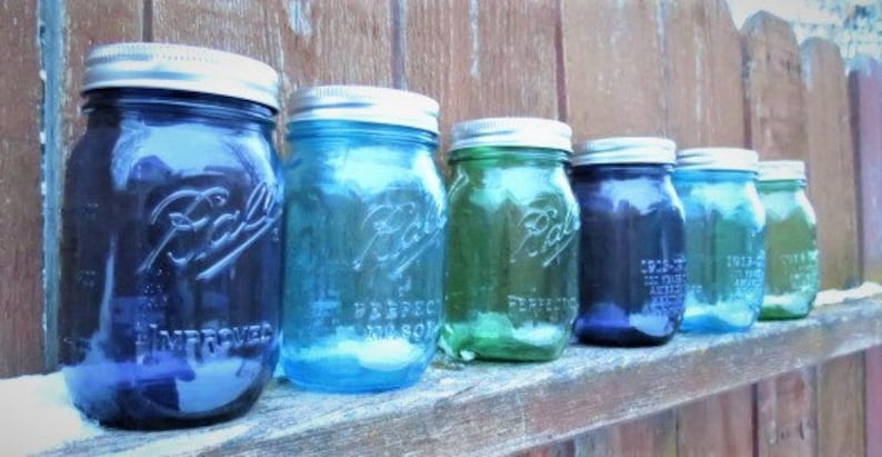 May include: A row of vintage Ball mason jars in various shades of blue and green, with silver lids. The jars are arranged on a wooden surface, showcasing their embossed lettering and classic design. The jars are filled with a clear liquid.