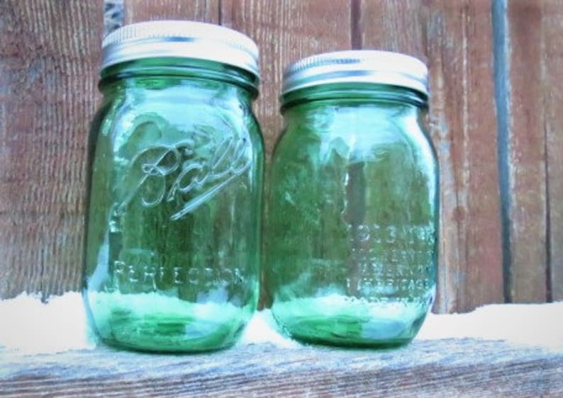 May include: Two green Ball mason jars with silver lids. The jars are embossed with the Ball logo and the word "PERFECTION". The jars are sitting on a wooden surface.
