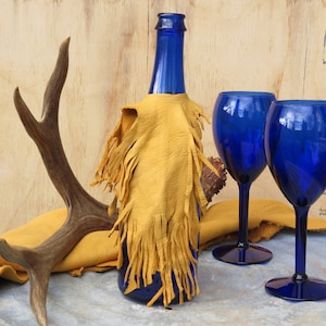 May include: A blue glass bottle with a yellow leather fringe wrap, two blue glass wine glasses, and a brown antler on a wooden surface.