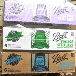 May include: Three boxes of Ball Vintage Style Jars, each containing six jars. The boxes are purple, white, and brown, with the Ball logo and text. The purple box is a limited edition. Each box features a jar illustration and text indicating the 100th anniversary.