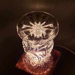 Puede incluir: Una l&aacute;mpara de cristal con base de madera. El cristal es transparente y tiene un patr&oacute;n de estrella. La base es de madera oscura.