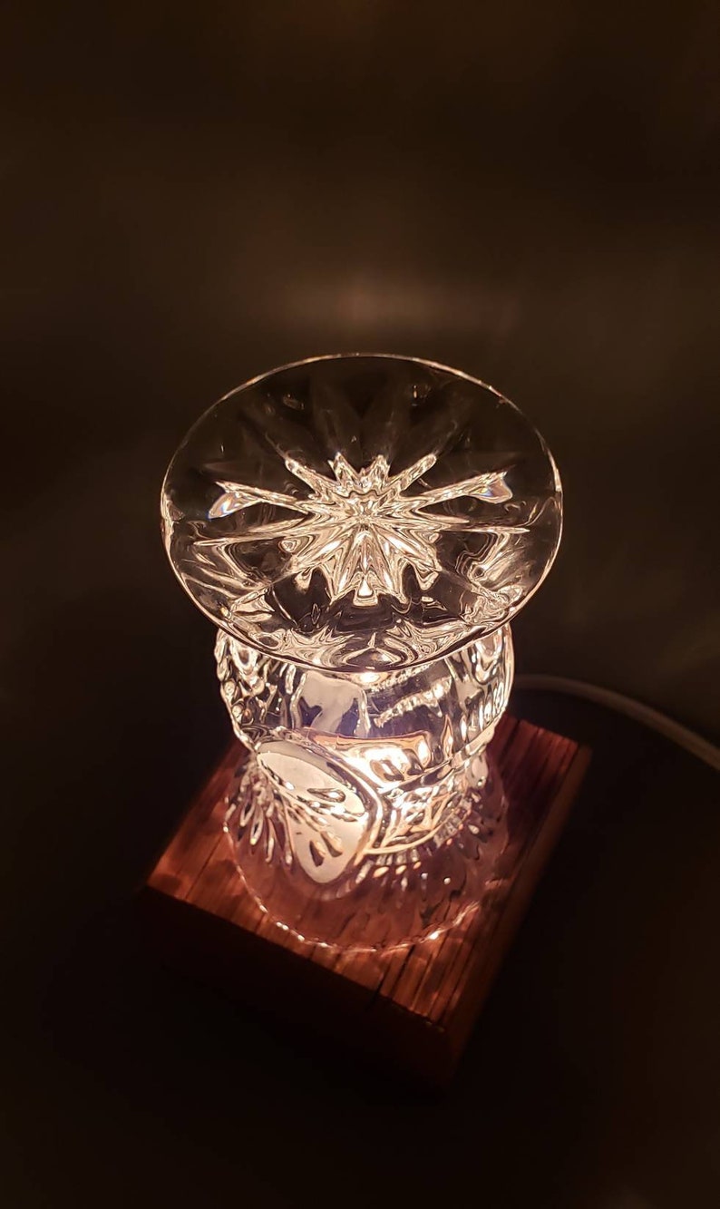 Puede incluir: Una l&aacute;mpara de cristal con base de madera. El cristal es transparente y tiene un patr&oacute;n de estrella. La base es de madera oscura.