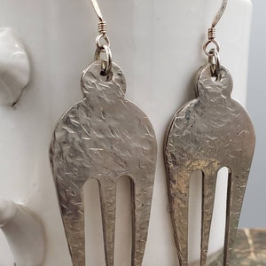 May include: A pair of silver fork earrings with a hammered texture. The earrings are made from recycled silverware and have a unique, rustic look.