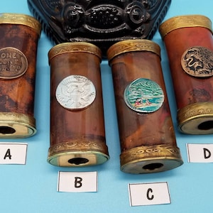 May include: Four decorative wooden tubes with different coin designs on the top. The tubes are brown with gold trim and have a hole at the bottom. The coins are a US penny, a US silver dollar, a coin with a mountain scene, and a coin with an eagle design.