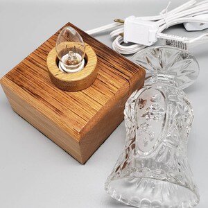 Puede incluir: Una base de l&aacute;mpara de madera con una pantalla de vidrio transparente. La l&aacute;mpara tiene una bombilla y un cable blanco.