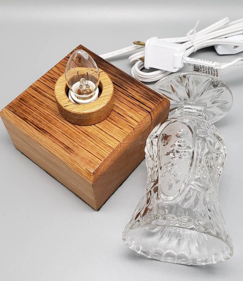 Puede incluir: Una base de l&aacute;mpara de madera con una pantalla de vidrio transparente. La l&aacute;mpara tiene una bombilla y un cable blanco.