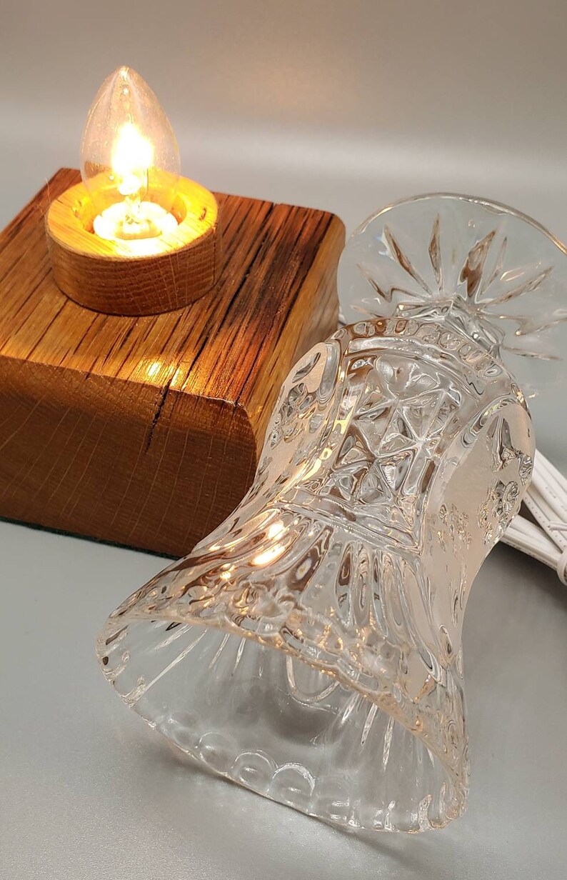 Puede incluir: Una peque&ntilde;a base de l&aacute;mpara de madera con una pantalla de vidrio transparente. La pantalla tiene un dise&ntilde;o decorativo de vidrio cortado. Una bombilla est&aacute; encendida dentro de la pantalla.