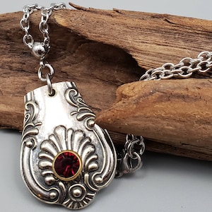 May include: A silver necklace with a pendant made from a vintage spoon. The pendant features an ornate design and a red gemstone in the center.