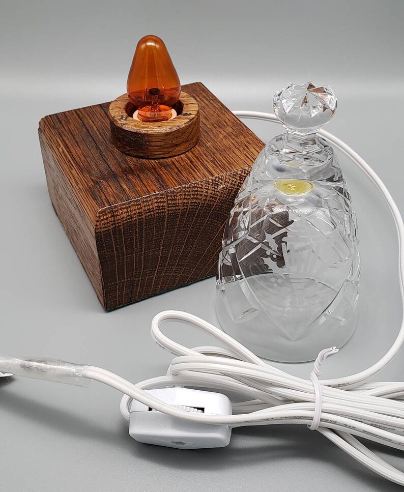 May include: A small table lamp with a wooden base and a clear glass shade. The lamp has an orange light bulb and a white cord with a switch.