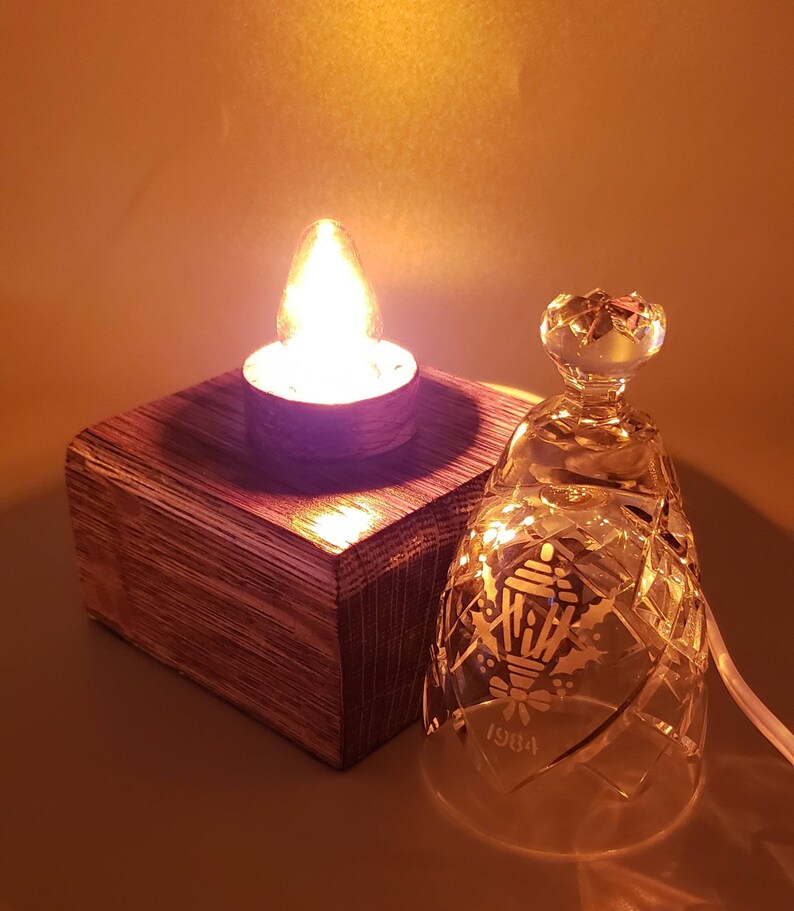 May include: A wooden base with a lit candle and a clear glass bell with a holly and lantern design and the year 1984 etched on the side.