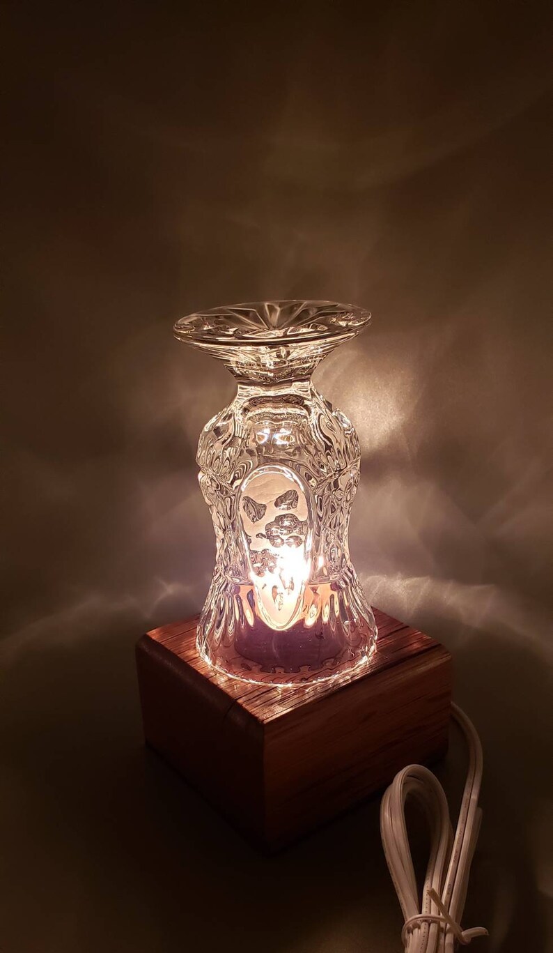 Puede incluir: Una peque&ntilde;a l&aacute;mpara de vidrio transparente con un dise&ntilde;o texturizado se asienta sobre una base de madera. La l&aacute;mpara est&aacute; encendida y emite un brillo c&aacute;lido.
