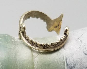 May include: A gold-toned ring with a decorative, wave-like design. The ring is open and appears to be made of metal.