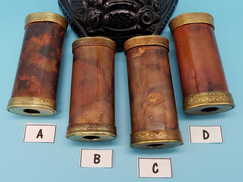 May include: Four antique brass-colored tubes with gold-colored trim and a decorative pattern. The tubes are labeled A, B, C, and D.
