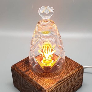 May include: A crystal glass lampshade with a gold design sits on a dark brown wooden base. The lampshade is lit from within, casting a warm glow.