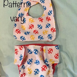 May include: A pink baby diaper and bib with a red trim and a pattern of blue, yellow, and red anchors. The text "Patterns vary" is visible in the image.