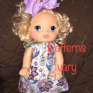 May include: A doll with blonde curly hair wearing a purple bow and a white dress with a paisley pattern. The text "Patterns vary" is visible in the image.