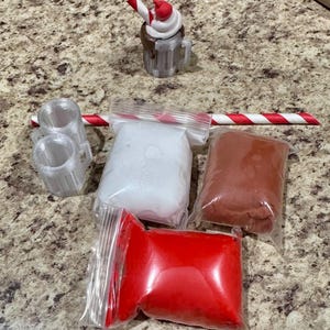 May include: A miniature dessert-themed craft kit featuring a small mug with whipped cream and a cherry, two small mugs, a red and white striped straw, and bags of white, red, and brown materials.