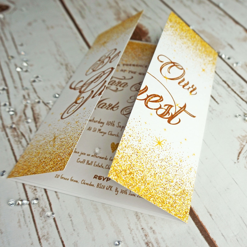 Puede incluir: Invitaci&oacute;n de boda con purpurina dorada y el texto "Our Best" en letra cursiva. La invitaci&oacute;n est&aacute; doblada en tres partes y tiene un fondo blanco.