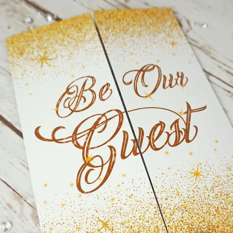Puede incluir: Un cartel de cartulina blanca con fondo de purpurina dorada y letras de cobre que dicen "Be Our Guest".