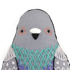 May include: A gray fabric bird with embroidered details. The bird has a white beak, black eyes, and a colorful pattern on its chest.