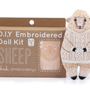 May include: A brown cardboard box with a white label that says "D.I.Y Embroidered Doll Kit Level 3 SHEEP kiriki (embroidery)". The box contains a kit to make a sheep doll. A finished sheep doll is shown next to the box. The sheep doll is wearing a white sweater and has a brown face.