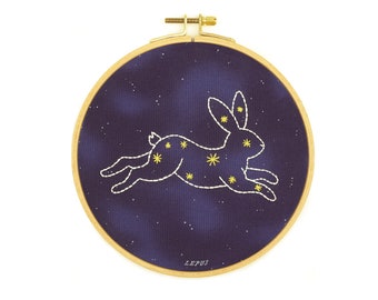 May include: A dark blue embroidery hoop with a white outline of a rabbit constellation with yellow stars. The text "LEPUS" is printed on the hoop.
