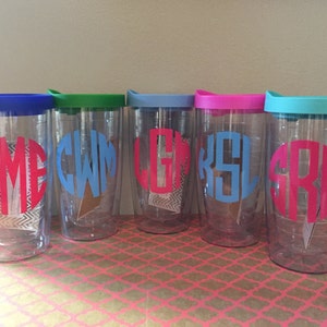 May include: Five clear plastic tumblers with lids in various colors, each with a different monogram in a contrasting color. The monograms are "YME", "CWM", "LGK", "KSL", and "SRH".