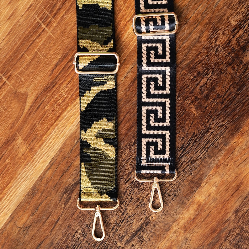 May include: Two black and gold patterned straps with gold metal clasps. The strap on the left has a camouflage pattern. The strap on the right has a Greek key pattern.