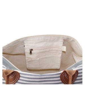 Pu&ograve; includere: Vista interna di una borsa tote in tela a righe con una tasca con cerniera e manici in pelle.