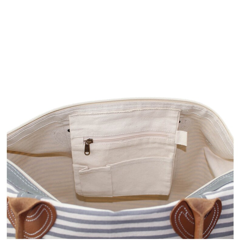 Pu&ograve; includere: Vista interna di una borsa tote in tela a righe con una tasca con cerniera e manici in pelle.