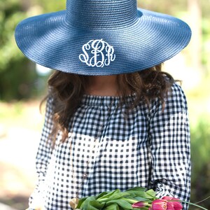 May include: A navy blue sun hat with a wide brim and a white monogram. The hat is worn by a person holding a bouquet of pink tulips.