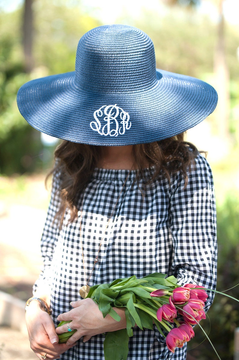 May include: A navy blue sun hat with a wide brim and a white monogram. The hat is worn by a person holding a bouquet of pink tulips.