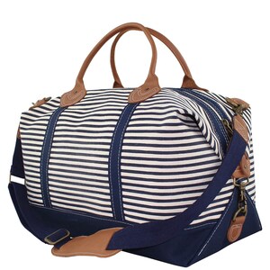 Pu&ograve; includere: Una borsa da viaggio in tela a righe blu navy e bianche con manici in pelle marrone e una tracolla regolabile blu navy.