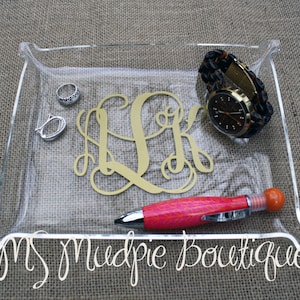 May include: Clear acrylic tray with gold monogram, rings, a watch, and a pink and orange pen. The tray has a curved edge and the text "MS Mudpie Boutique" is written on the bottom.