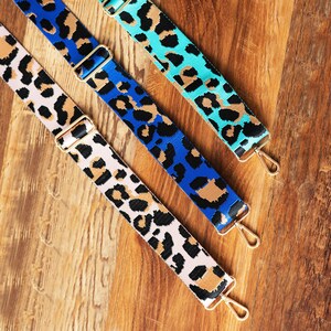 May include: Three colorful leopard print fabric straps with gold metal hardware. The straps are blue, pink, and turquoise.