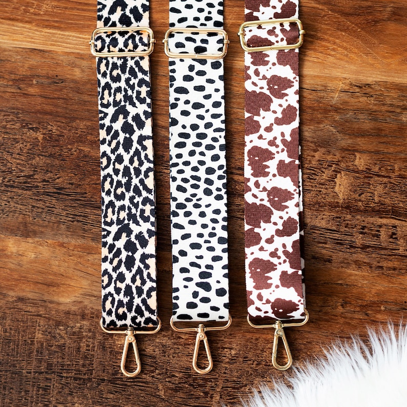 May include: Three different patterned fabric straps with gold metal clasps. The straps are leopard print, black and white polka dot, and brown and white cow print.