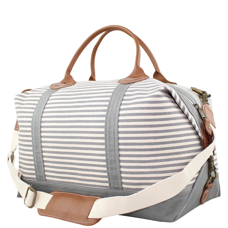 Pu&ograve; includere: Una borsa da viaggio in tela a righe e pelle per il fine settimana con manico superiore e una lunga tracolla regolabile. La borsa &egrave; grigia e bianca con dettagli in pelle marrone.