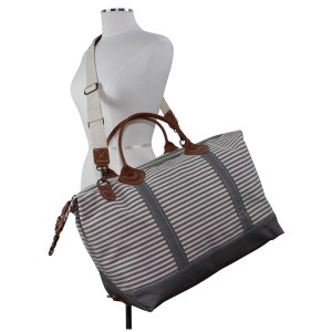 Pu&ograve; includere: Una borsa da viaggio in tela a righe con dettagli in pelle marrone e una lunga tracolla regolabile. La borsa ha una chiusura a zip e due manici superiori.