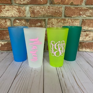 May include: Four reusable cups with different colors and personalized designs. The cups are light blue, white, green, and dark green. The white cup has the name "Maren" written in pink. The green cup has a monogram in pink.