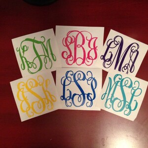 May include: Six white square stickers with different colored monogram initials. The monograms are in a script font. The colors are green, pink, purple, yellow, blue, and teal.
