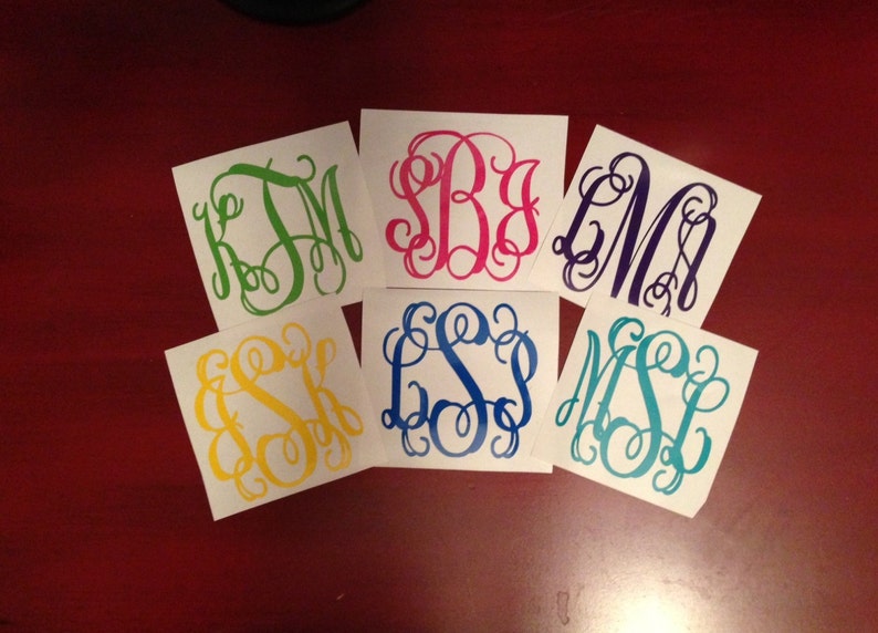 May include: Six white square stickers with different colored monogram initials. The monograms are in a script font. The colors are green, pink, purple, yellow, blue, and teal.