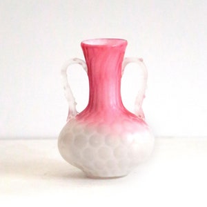 May include: A small, white and pink glass vase with two handles. The vase has a textured, bubble-like surface and a pink ombre effect.