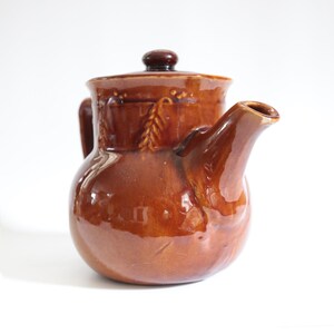 May include: A brown ceramic teapot with a lid and a spout. The teapot has a floral design.