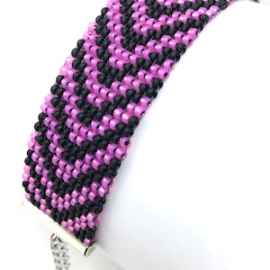 May include: A pink and black beaded bracelet with a silver clasp. The bracelet is made with small, round beads and has a chevron pattern.