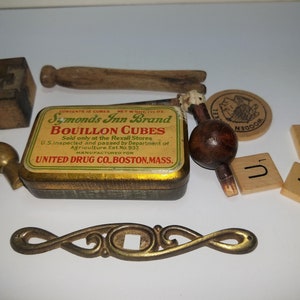 May include: An assortment of vintage items, including a bouillon cube tin, wooden blocks, a keyhole, and decorative hardware. The tin reads "Symonds Inn Brand Bouillon Cubes". Other items include wooden game tiles with letters.
