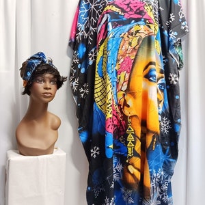 May include: A black kaftan with a colorful print of a woman's face and snowflakes. The kaftan has short sleeves and a loose fit. It is paired with a blue and white patterned head wrap.