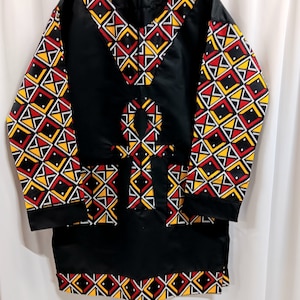 May include: Black long-sleeved shirt with a geometric pattern in red, yellow, and white. The shirt features a large Ankh symbol in the center.